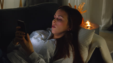 Woman-Lying-On-Sofa-At-Home-At-Night-Streaming-Or-Looking-At-Online-Content-On-Mobile-Phone